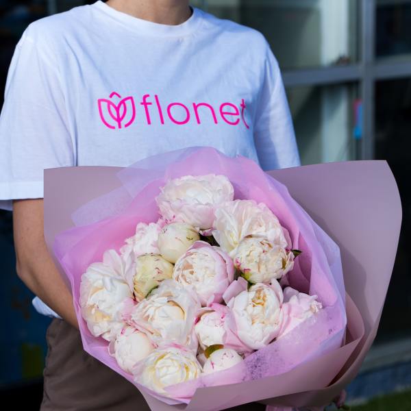 Person holding a bouquet of pale pink and white peonies wrapped in pink paper