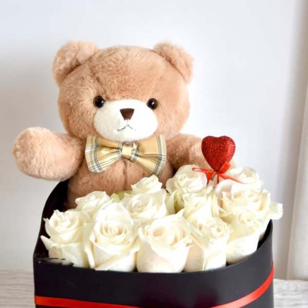 Teddy bear in a box with white roses and a red heart pick