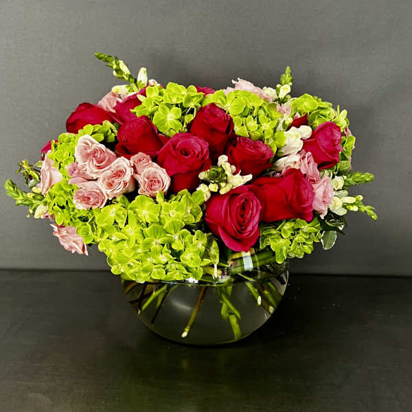 Red and pink roses arranged with bright green hydrangeas in a glass bowl vase.