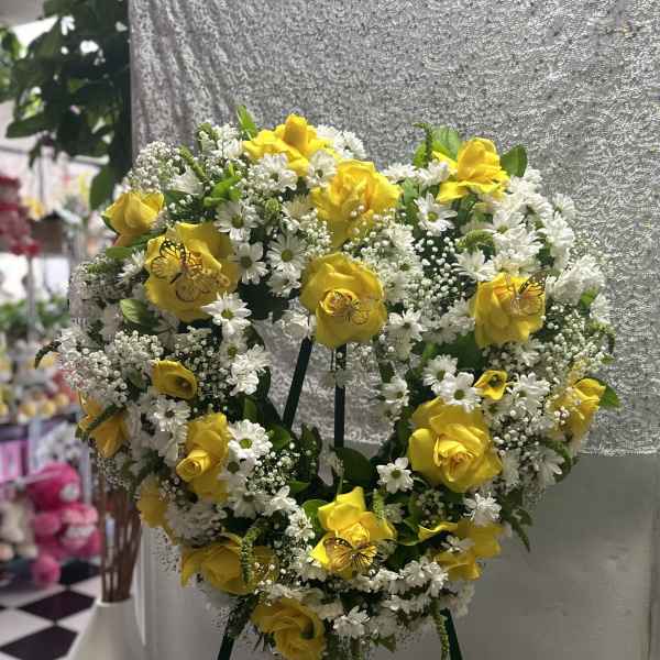 Heart-shaped floral wreath with yellow roses and white daisies on an easel