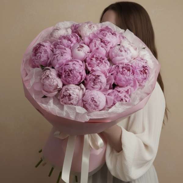 Large bouquet of pink peonies wrapped in pink paper with a white ribbon