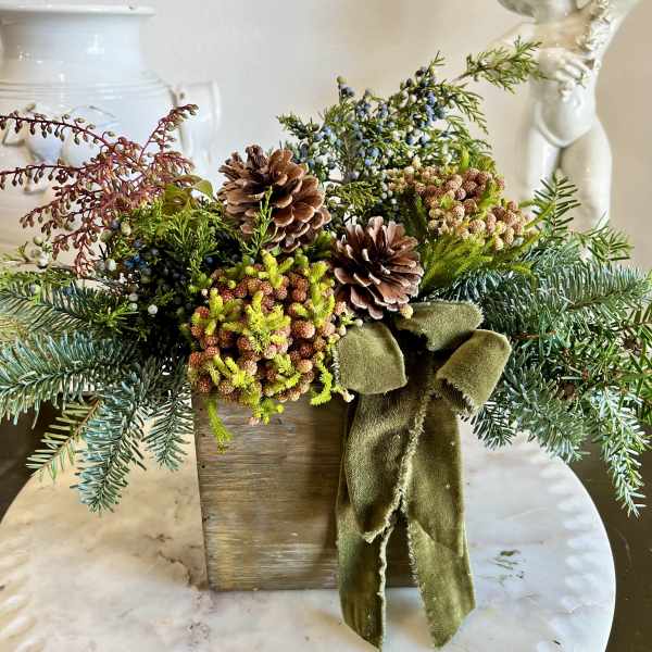 Rustic evergreen arrangement with pinecones and a green ribbon in a wooden box