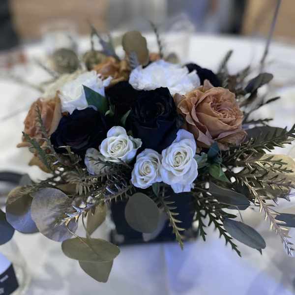 Low centerpiece of white, tan, and dark roses in a black square vase