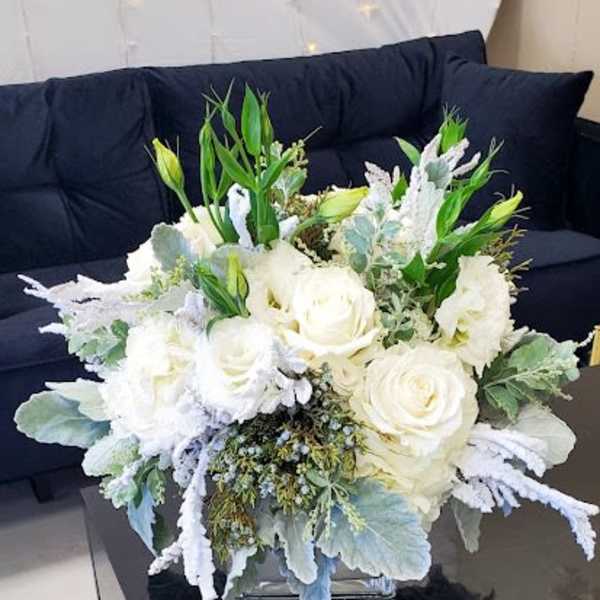 Low white rose and lisianthus arrangement in a clear glass cube vase.