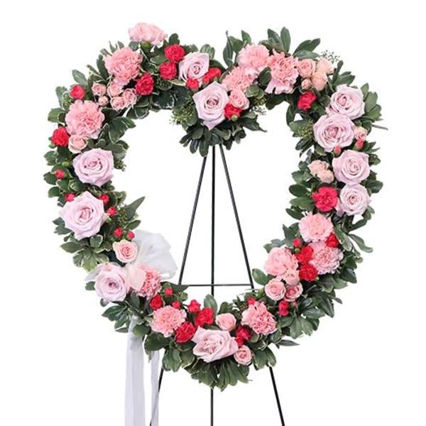 Heart-shaped floral wreath with pink and red roses on a stand