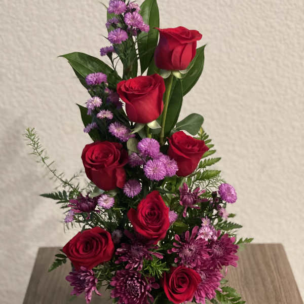 Red roses and purple flowers in a clear glass vase