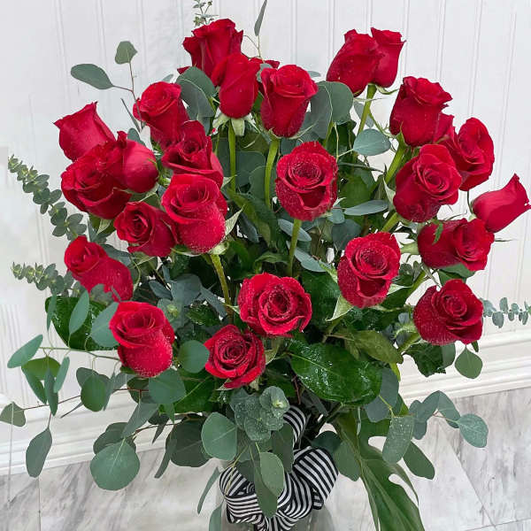 Tall arrangement of long-stemmed red roses in a clear glass vase with striped ribbon