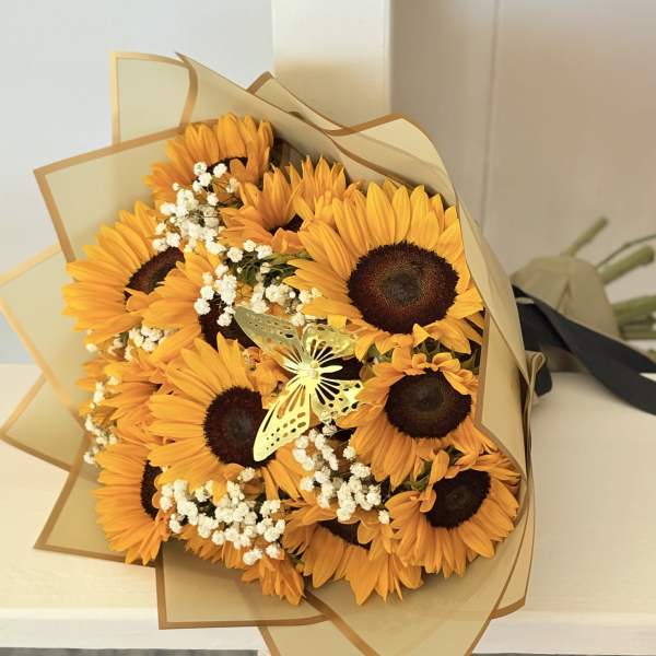 Bouquet of orange sunflowers with white filler flowers wrapped in tan paper