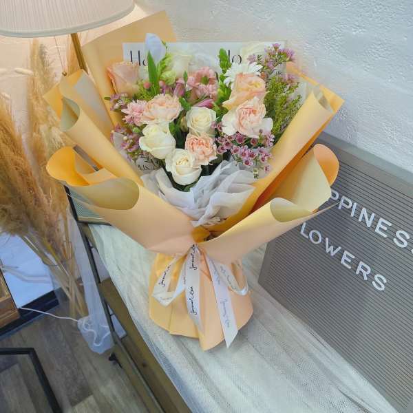 Bouquet of pale pink and white flowers wrapped in peach paper