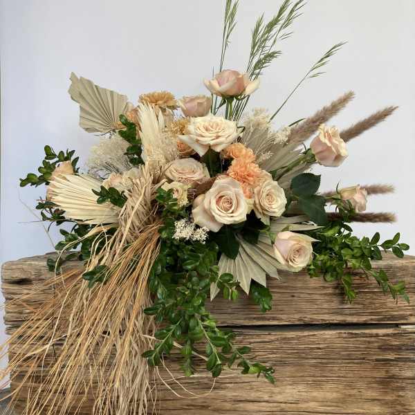 Blush roses arranged with dried grasses and fan-shaped palm leaves on wood