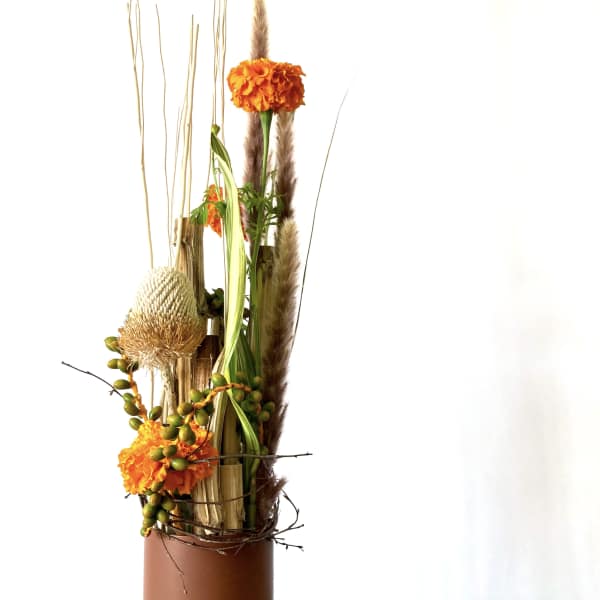 Orange floral arrangement in a brown vase with tall dried accents
