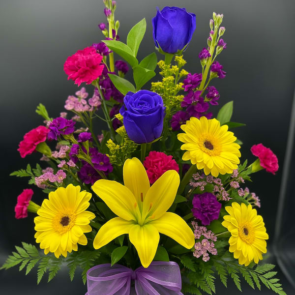 Tall mixed bouquet with yellow daisies and lily, blue roses, pink carnations in glass vase with purple bow