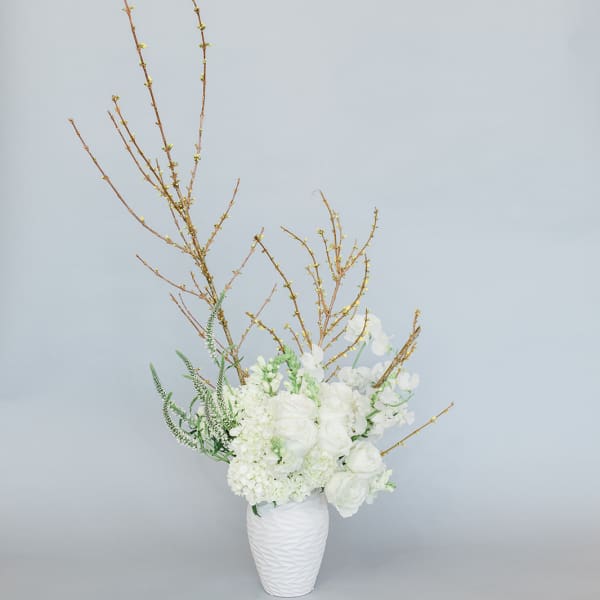 White floral arrangement in a textured white vase with tall branches