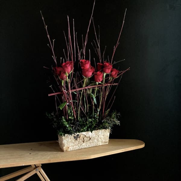 Red roses arranged in a rectangular stone planter with tall twigs