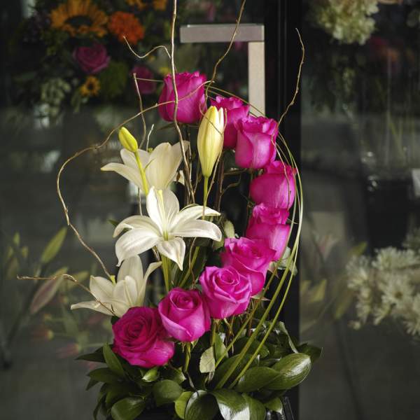 Pink roses and white lilies in a tall black container with curly branches