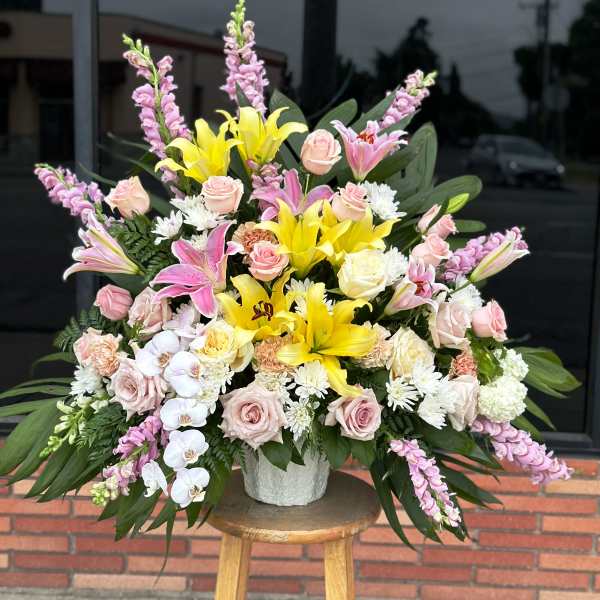 Large mixed bouquet with yellow lilies, pink roses, and orchids in a white vase