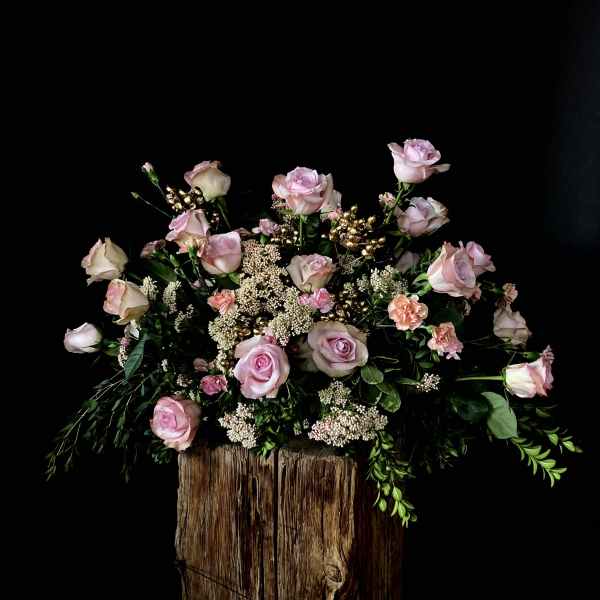 Pink roses and small filler flowers arranged on a rustic wood base