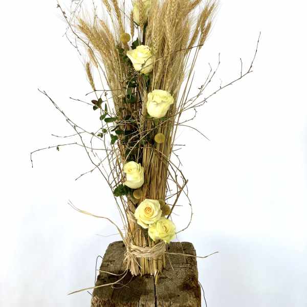 Tall arrangement of pale yellow roses with dried grasses on a wood base