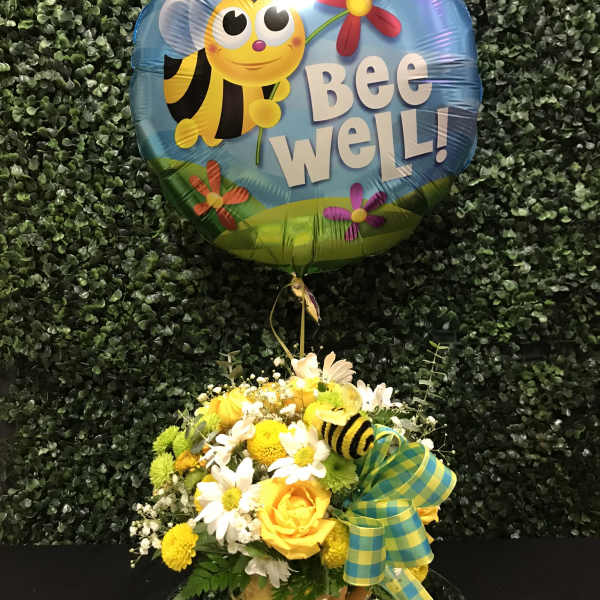 Bee Well balloon above a yellow and white flower arrangement in a vase