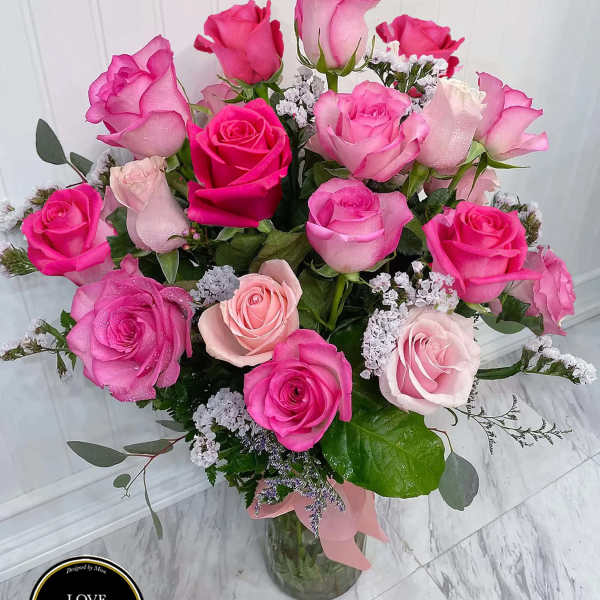 Tall glass vase of hot pink and light pink roses with white filler flowers and a pink ribbon