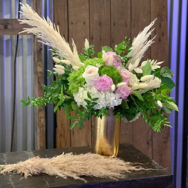 Pink and white floral arrangement in a gold vase with pampas grass