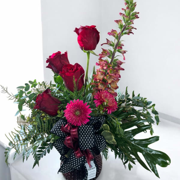 Red roses and pink flowers in a black polka-dot vase with ribbon