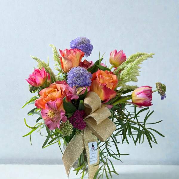 Bouquet of pink and orange roses with purple blooms in a glass vase