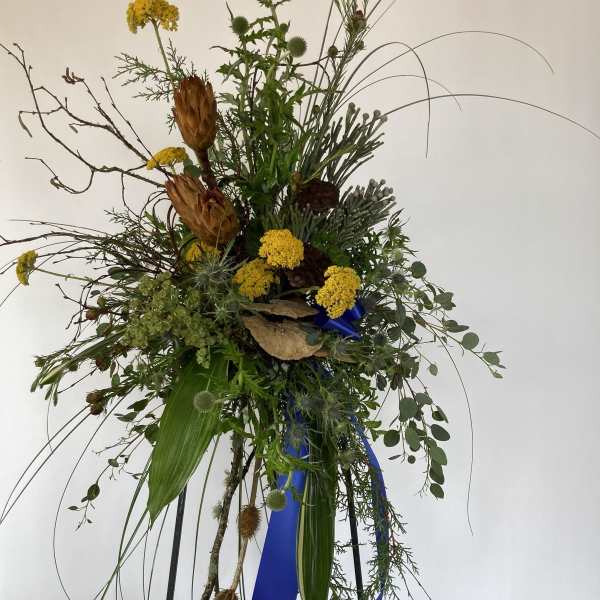 Tall wildflower arrangement with yellow blooms and dried seed pods on a stand