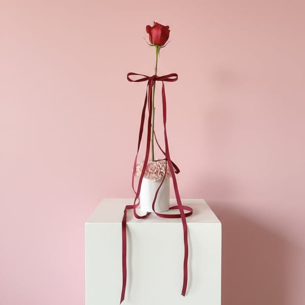 Single red rose in a white vase with burgundy ribbon