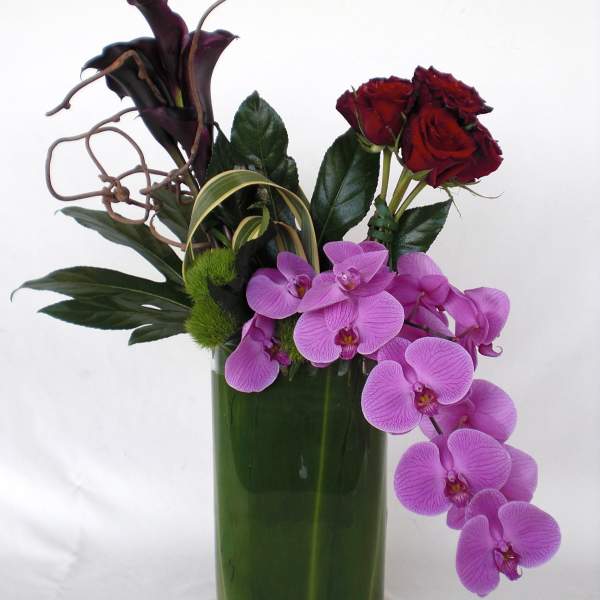 Arrangement of red roses, purple orchids, and dark calla lilies in a green vase