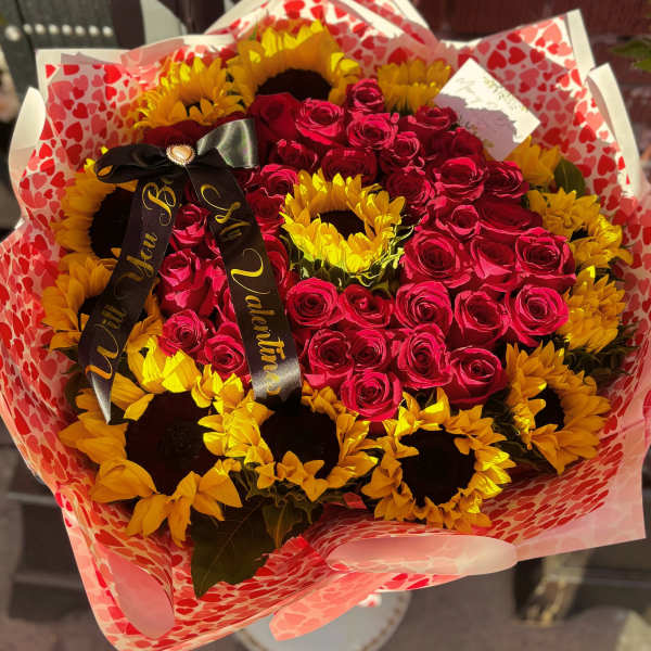 Bouquet of red roses and yellow sunflowers wrapped in heart-patterned paper