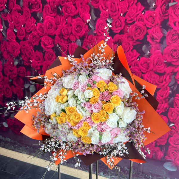 Large bouquet of white, pink, and yellow roses with orange wrapping
