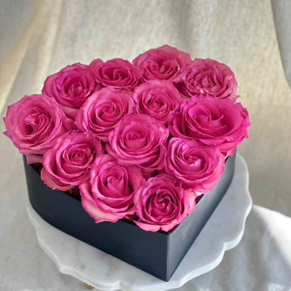 Pink roses arranged in a black heart-shaped box