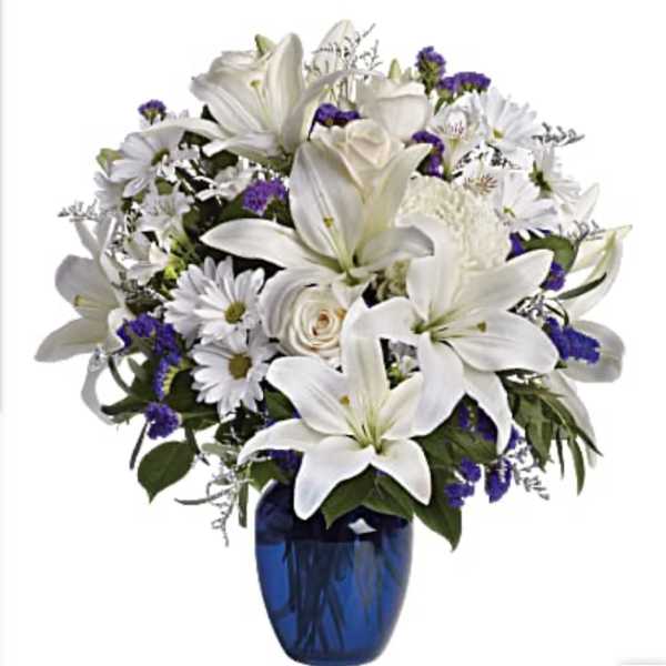 White lilies and daisies arranged in a blue vase with purple accents