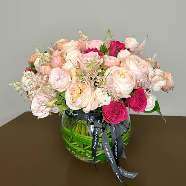 Pink and white rose bouquet in a round glass vase with ribbon