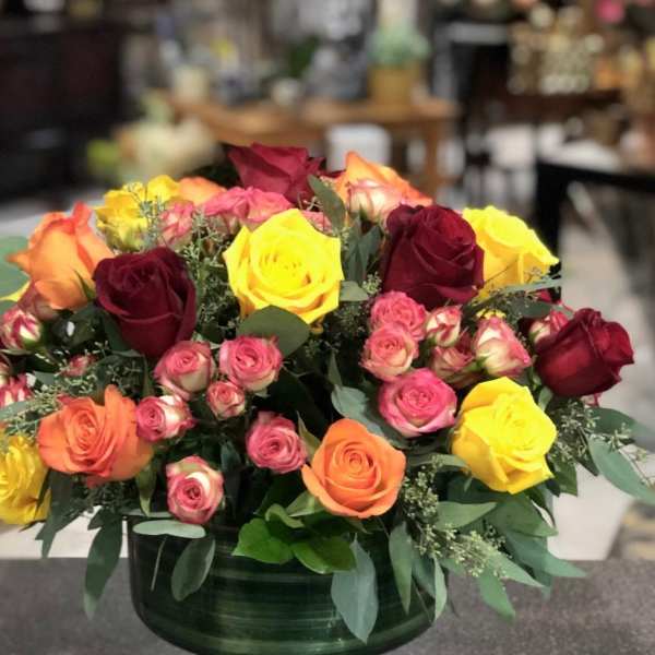Mixed roses in a low green vase with pink, yellow, orange, and burgundy blooms