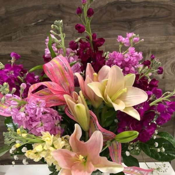 Pink and cream lilies with purple flowers in a glass vase