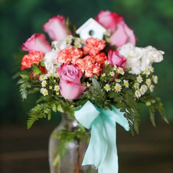 Pink roses and carnations in a glass vase with a blue ribbon