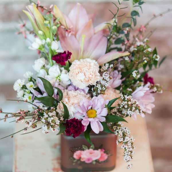 Pastel bouquet in a square vase with lilies, daisies, and carnations