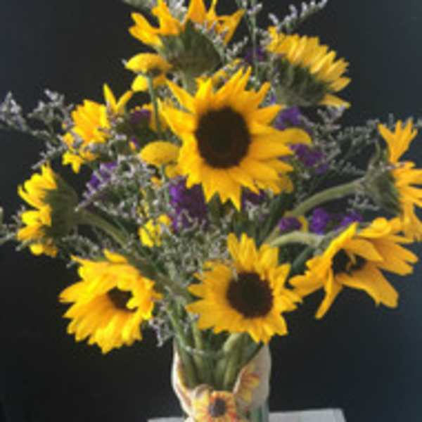 Bouquet of yellow sunflowers with purple accents in a clear vase