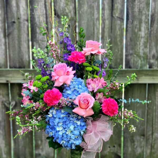 Pink and blue floral arrangement in a glass vase with a ribbon bow