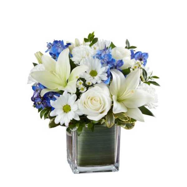 Short white and blue flower arrangement with lilies, roses, and daisies in a clear cube vase
