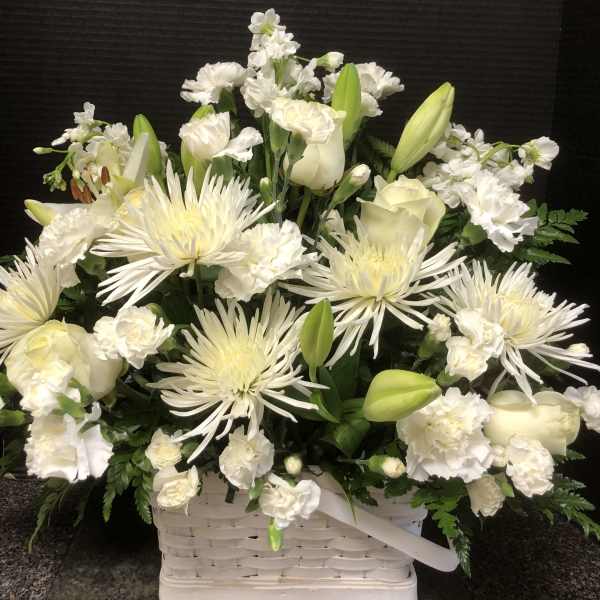 White floral arrangement in a white basket with lilies and spider mums