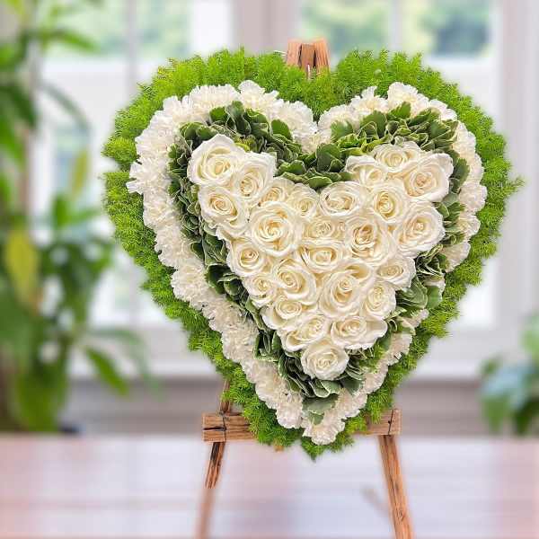 Heart-shaped floral arrangement of white roses and green hydrangeas on an easel
