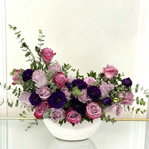 Pink and lavender roses arranged in a white bowl vase