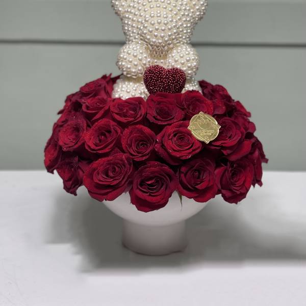 Red rose arrangement with a pearl teddy bear topper in a white vase