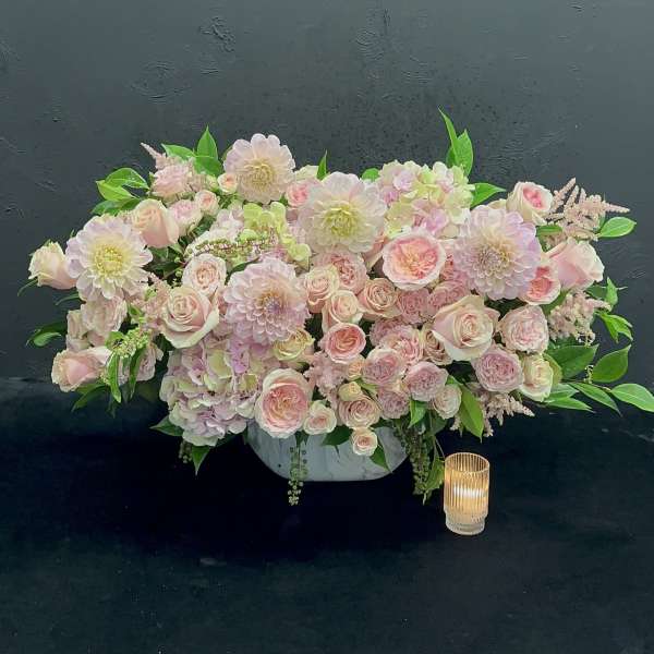 Low pastel floral centerpiece in a white bowl with a candle beside it