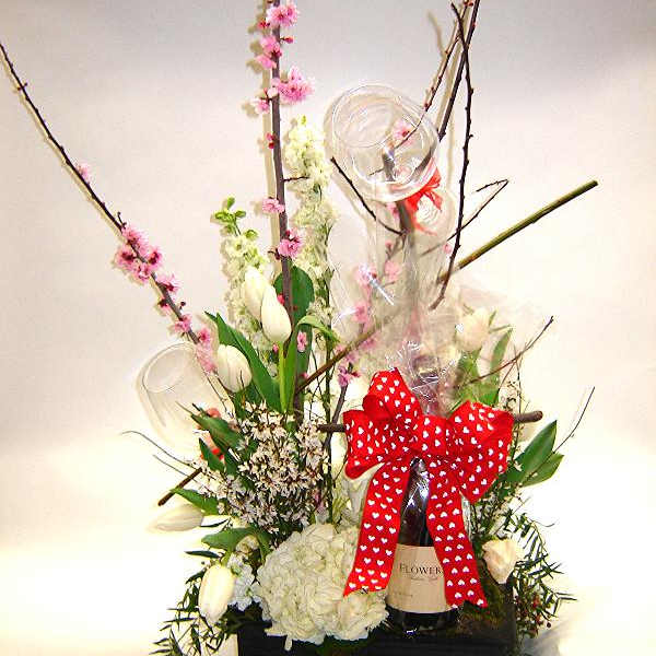 Tall floral gift arrangement with white blooms, pink blossoms, and a red bow on a bottle