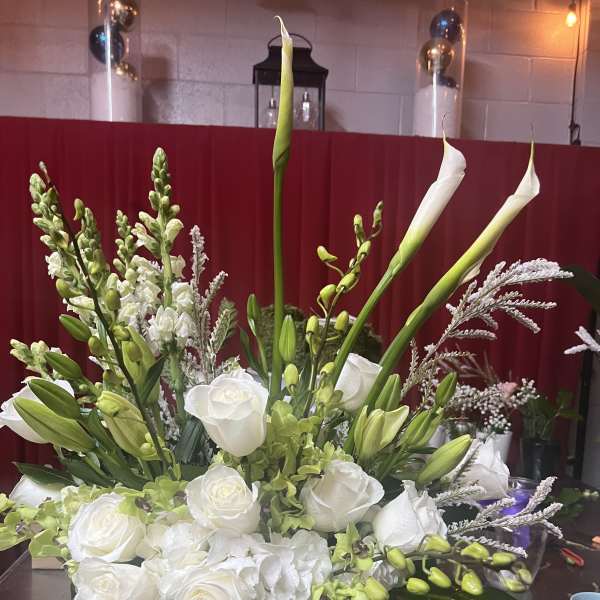 White roses and calla lilies in a white vase with green accents