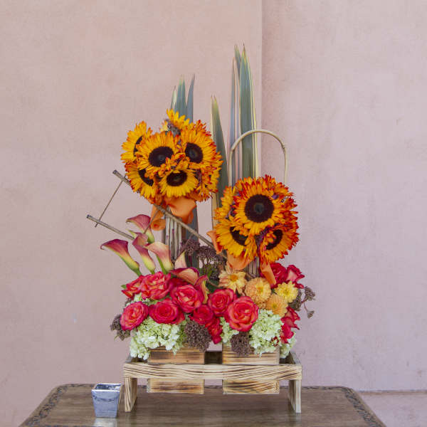 Tall floral arrangement with sunflowers, roses, and calla lilies in a wooden stand
